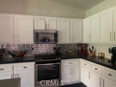 kitchen with white cabinets, backsplash, appliances with stainless steel finishes, and vaulted ceiling