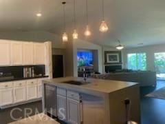 kitchen featuring decorative light fixtures, a kitchen island with sink, sink, and white cabinetry