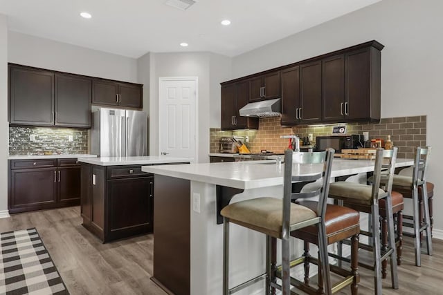 kitchen featuring decorative backsplash, a kitchen island, light hardwood / wood-style flooring, stainless steel refrigerator, and a breakfast bar area