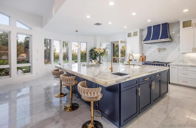 kitchen featuring tasteful backsplash, a kitchen island with sink, wall chimney range hood, and white cabinetry