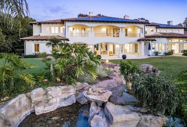 rear view of house featuring a lawn, a balcony, and a patio