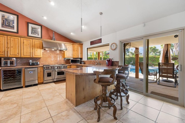 kitchen with high vaulted ceiling, wall chimney range hood, appliances with stainless steel finishes, a breakfast bar area, and beverage cooler