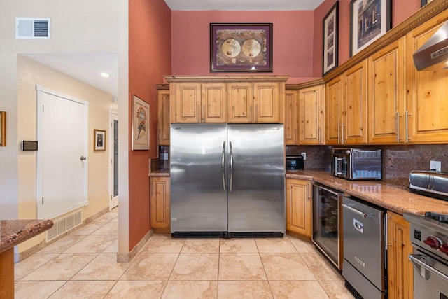 kitchen with backsplash, dark stone countertops, range hood, appliances with stainless steel finishes, and beverage cooler