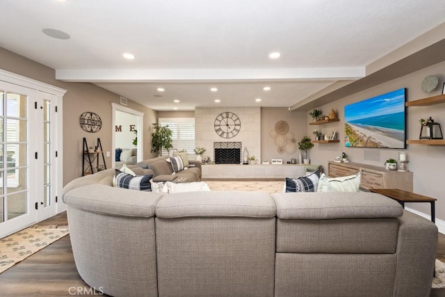 living room with beam ceiling, plenty of natural light, dark wood-type flooring, and a tiled fireplace