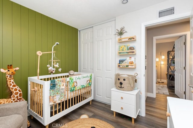 bedroom featuring wood walls, a closet, dark hardwood / wood-style floors, and a crib