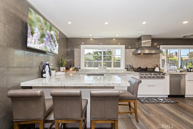 kitchen with a kitchen breakfast bar, light stone counters, dark wood-type flooring, wall chimney range hood, and white cabinetry