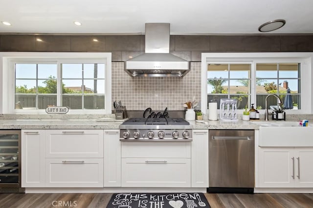 kitchen with wall chimney range hood, dark hardwood / wood-style floors, appliances with stainless steel finishes, white cabinetry, and beverage cooler