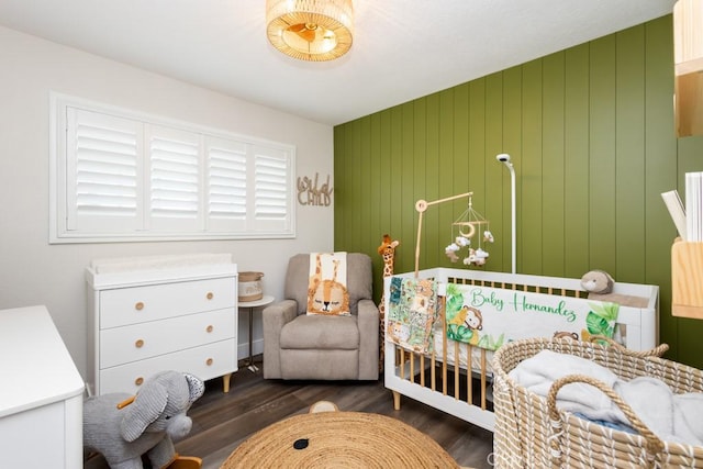 bedroom with wood walls, a crib, and dark wood-type flooring