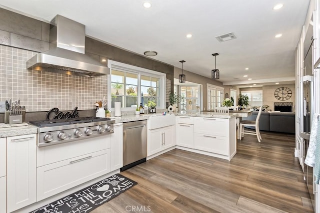 kitchen with white cabinets, stainless steel appliances, light stone counters, and wall chimney exhaust hood