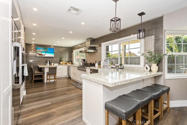 kitchen with decorative light fixtures, kitchen peninsula, dark wood-type flooring, and wall chimney range hood