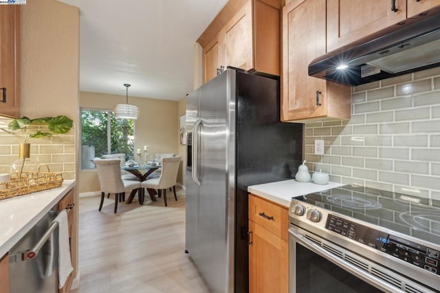 kitchen with tasteful backsplash, pendant lighting, light wood-type flooring, and appliances with stainless steel finishes