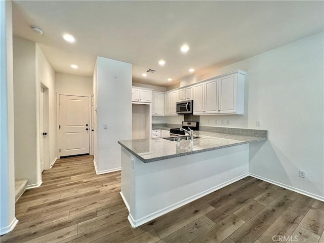 kitchen with white cabinets, kitchen peninsula, sink, and light hardwood / wood-style flooring