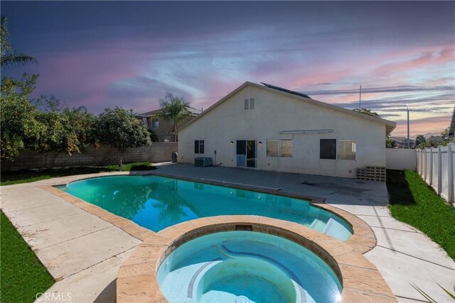 pool at dusk with a patio area and an in ground hot tub