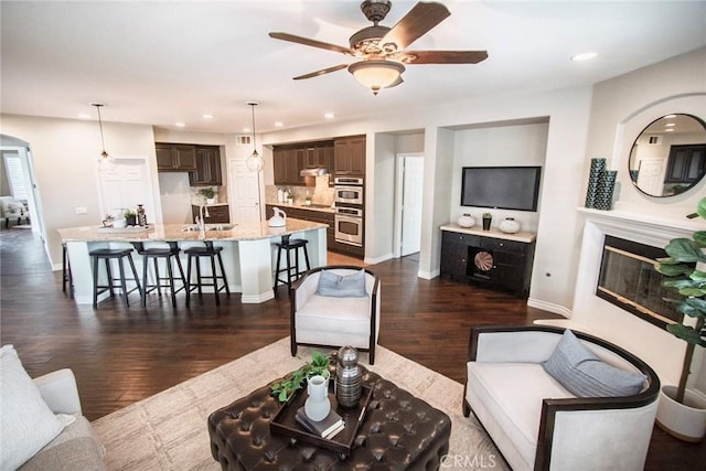 living room with ceiling fan, sink, and dark wood-type flooring