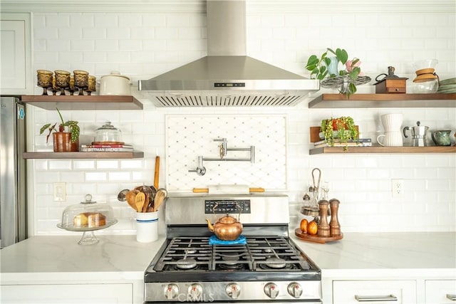 kitchen featuring decorative backsplash, gas stove, white cabinets, and wall chimney range hood