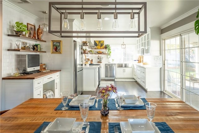 bar with white cabinetry, butcher block counters, stainless steel appliances, hanging light fixtures, and ornamental molding