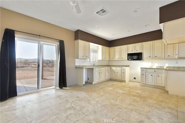 kitchen with cream cabinets, light stone counters, ceiling fan, and sink