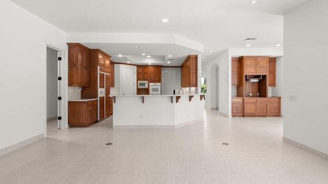 kitchen with a large island, light tile patterned flooring, a kitchen bar, and white appliances