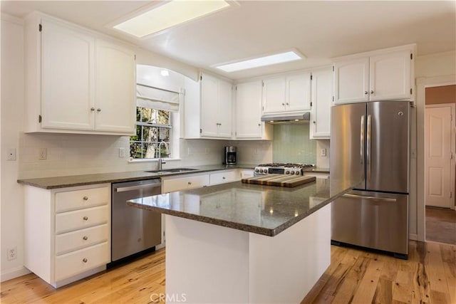 kitchen featuring a kitchen island, appliances with stainless steel finishes, dark stone counters, white cabinets, and light wood-type flooring