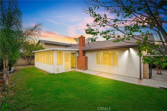 back house at dusk with a lawn and a sunroom