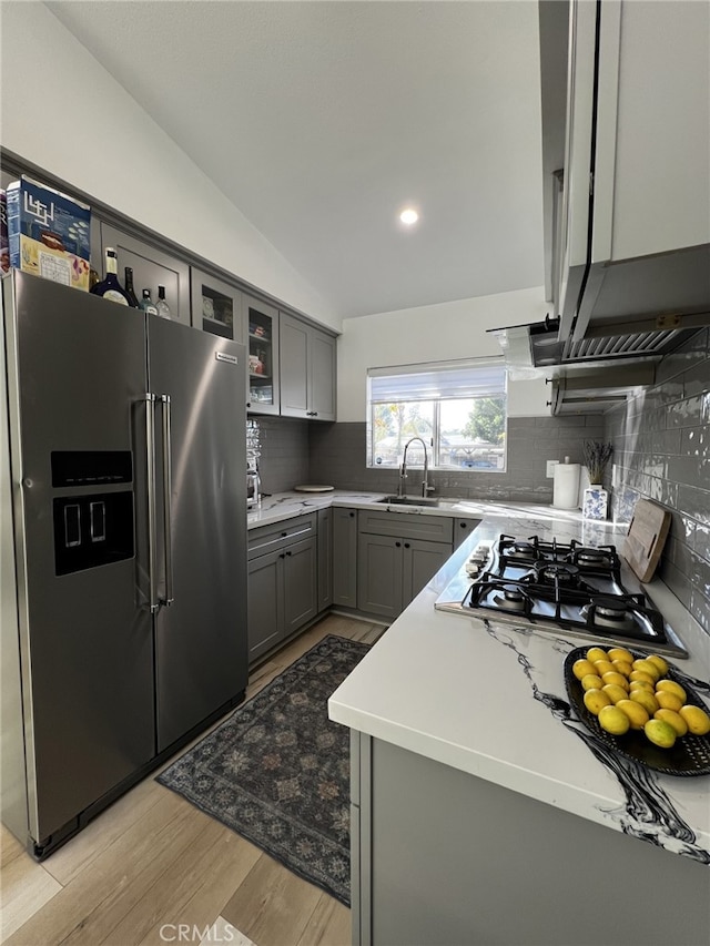 kitchen featuring decorative backsplash, appliances with stainless steel finishes, gray cabinetry, vaulted ceiling, and light hardwood / wood-style floors