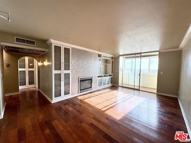 unfurnished living room with built in shelves, dark wood-type flooring, and crown molding