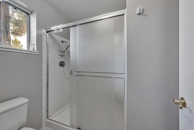 bathroom featuring a shower with door and toilet