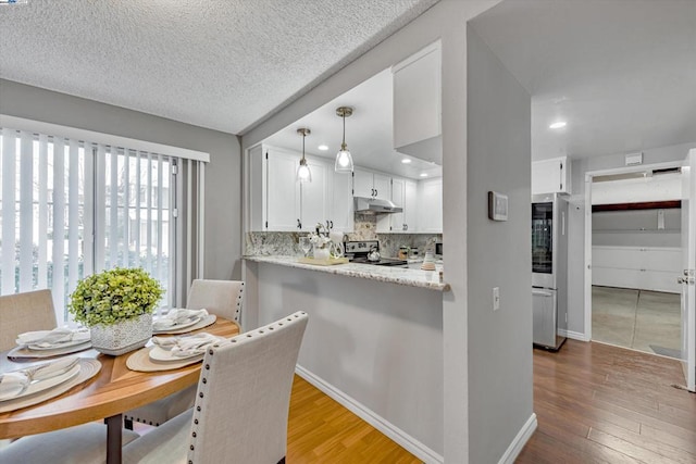 kitchen featuring tasteful backsplash, light hardwood / wood-style flooring, stainless steel range with electric cooktop, pendant lighting, and white cabinets