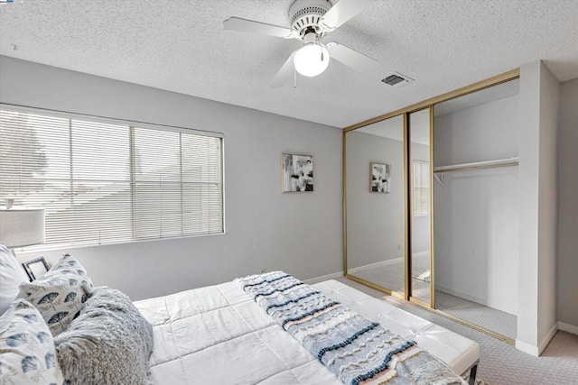 bedroom featuring ceiling fan, a closet, light colored carpet, and a textured ceiling