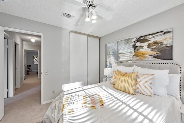 bedroom featuring a textured ceiling, a closet, ceiling fan, and light colored carpet