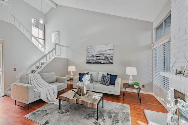 living room with beamed ceiling, high vaulted ceiling, wood-type flooring, and a brick fireplace