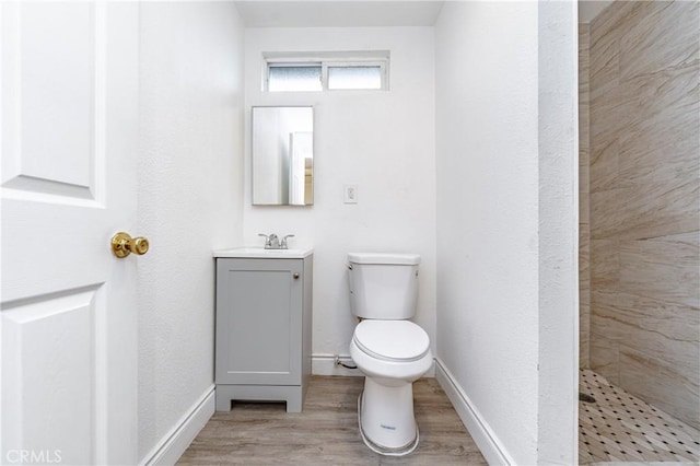 bathroom with hardwood / wood-style flooring, vanity, toilet, and a tile shower