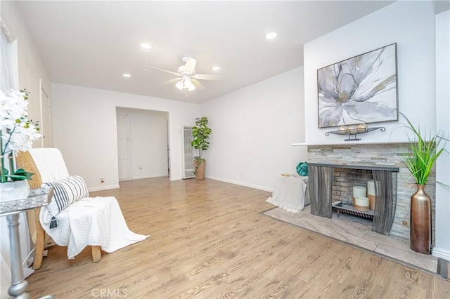 living area with ceiling fan, a fireplace, and light wood-type flooring