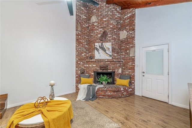 living room featuring beamed ceiling, wood-type flooring, a brick fireplace, and ceiling fan