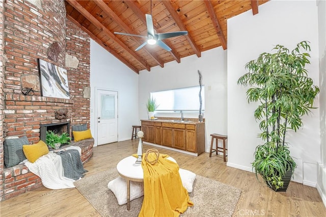 living room with beam ceiling, sink, high vaulted ceiling, a fireplace, and light wood-type flooring