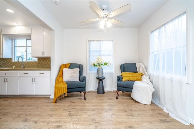 living area with a healthy amount of sunlight, ceiling fan, and light hardwood / wood-style floors