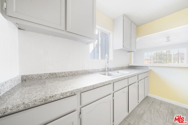 kitchen featuring decorative backsplash, white cabinetry, sink, and ceiling fan