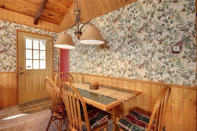 dining space featuring carpet, vaulted ceiling with beams, wooden ceiling, and wooden walls