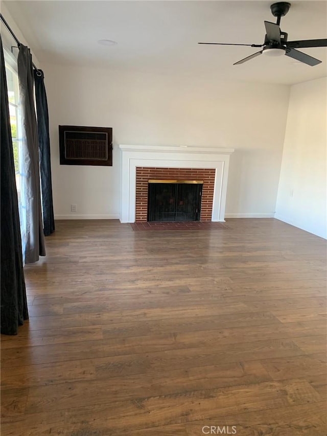 unfurnished living room with ceiling fan, dark hardwood / wood-style flooring, and a brick fireplace