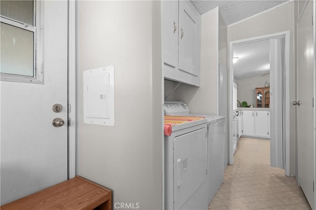 laundry room with electric panel, washing machine and dryer, a textured ceiling, and cabinets