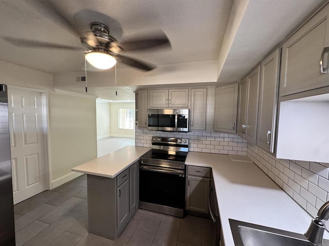 kitchen featuring ceiling fan, stainless steel appliances, tasteful backsplash, kitchen peninsula, and gray cabinets