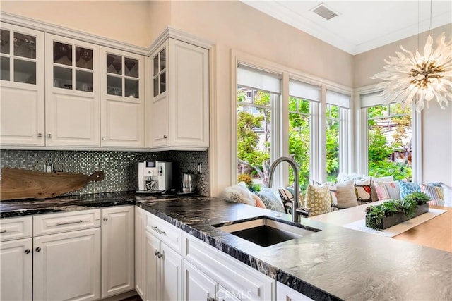 kitchen featuring pendant lighting, white cabinets, sink, ornamental molding, and tasteful backsplash