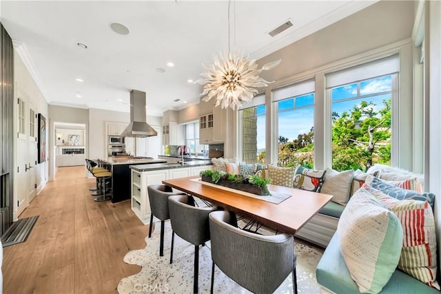 dining space with an inviting chandelier, light hardwood / wood-style floors, and ornamental molding