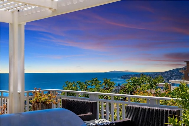 balcony at dusk featuring a water and mountain view