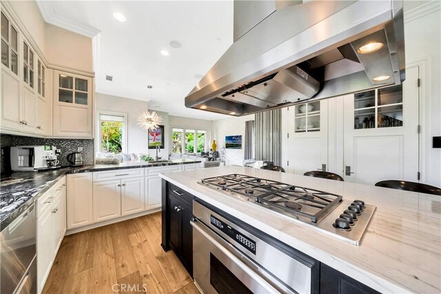 kitchen with tasteful backsplash, island exhaust hood, pendant lighting, appliances with stainless steel finishes, and light wood-type flooring