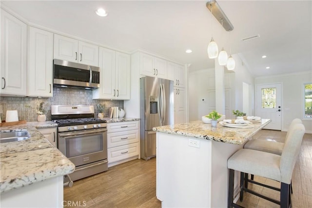 kitchen featuring ornamental molding, stainless steel appliances, light hardwood / wood-style floors, white cabinetry, and hanging light fixtures