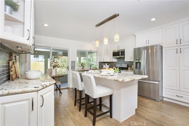 kitchen with white cabinets, backsplash, light hardwood / wood-style floors, and stainless steel appliances