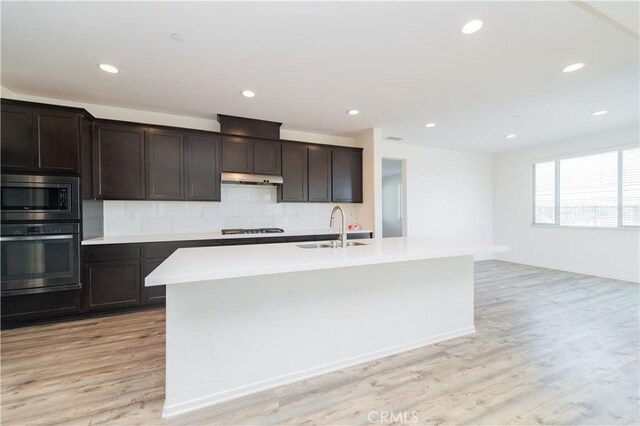 kitchen with appliances with stainless steel finishes, light hardwood / wood-style floors, a kitchen island with sink, and sink