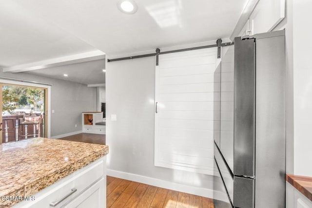 kitchen with light stone countertops, a barn door, white cabinets, light hardwood / wood-style floors, and stainless steel refrigerator