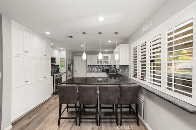 kitchen with a kitchen bar, white cabinets, appliances with stainless steel finishes, dark hardwood / wood-style flooring, and kitchen peninsula